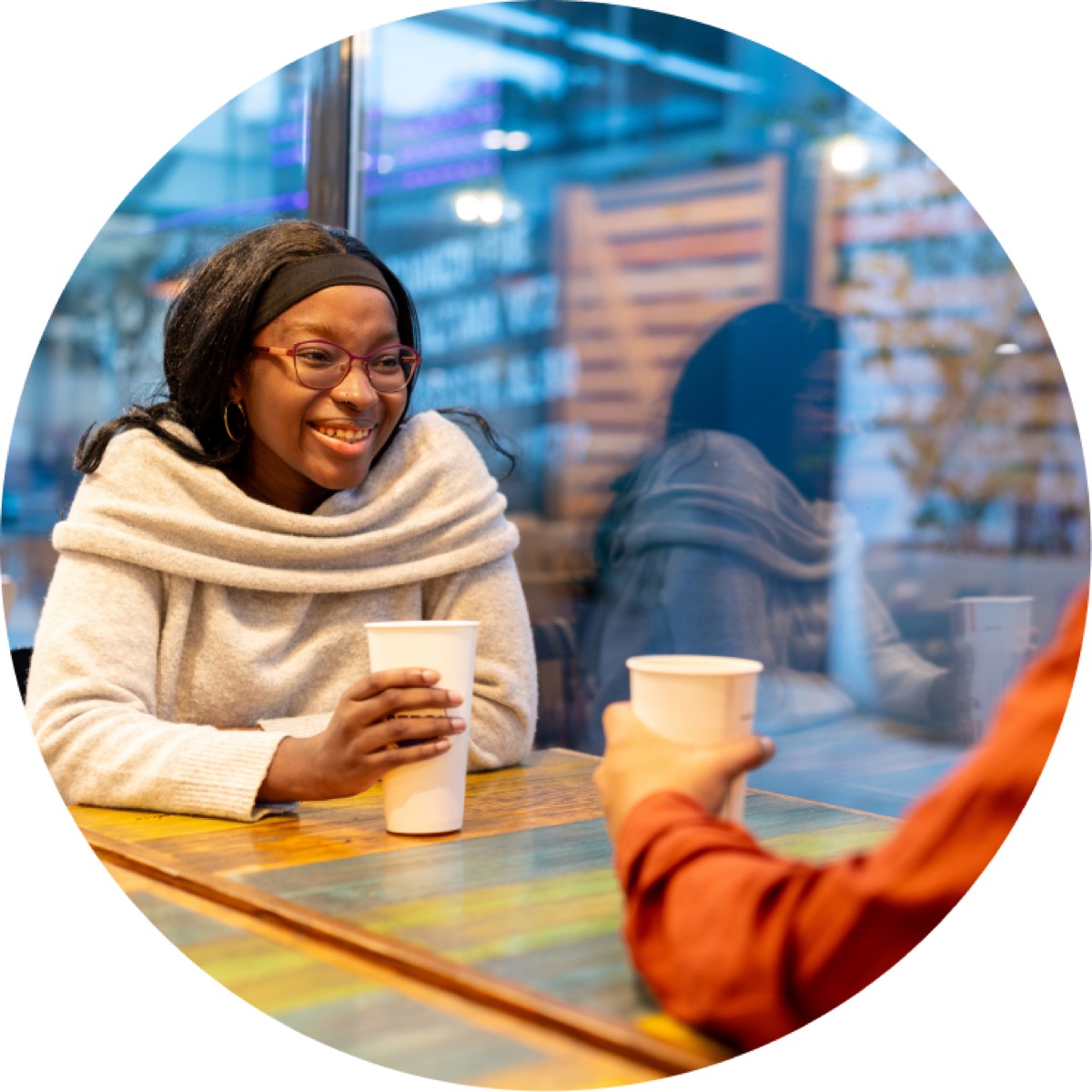 A woman smiling with a hot drink at a cafe table