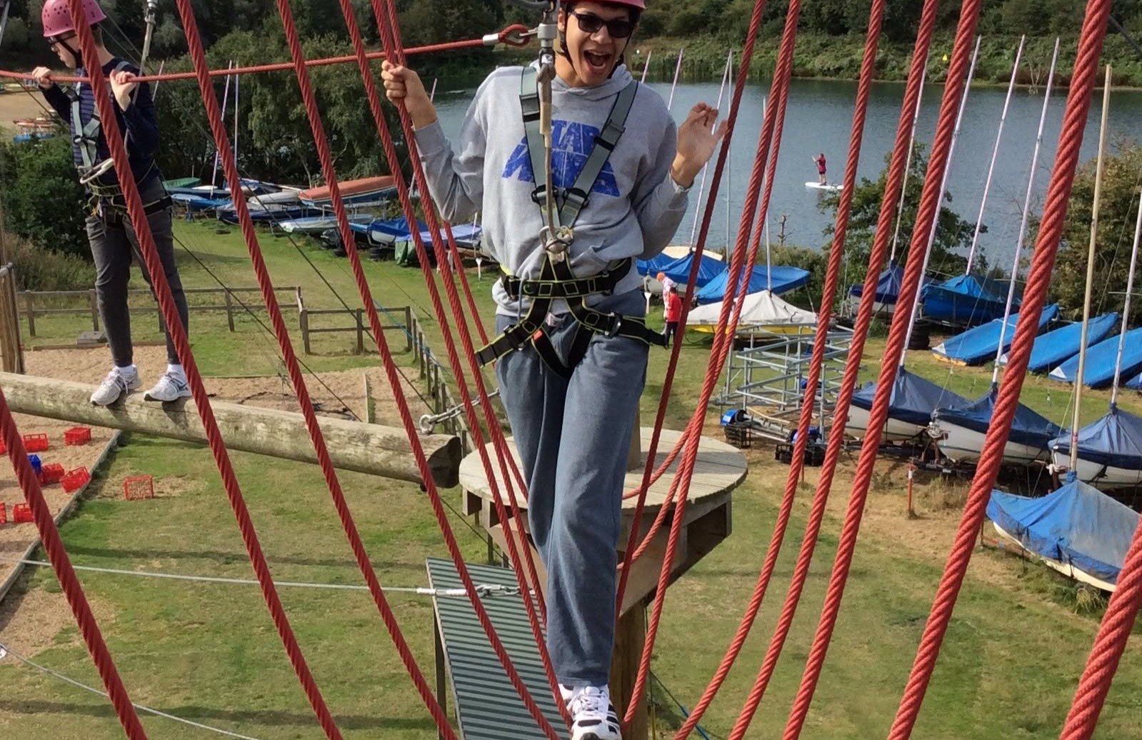 Young people in helmets and harnesses climbing a high-ropes course beside a lake